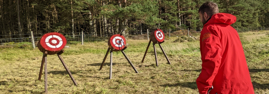a man in red jacket throwing axes at wooden axe targets