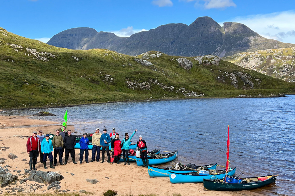 a group of adults stand by their canoes on a remote beach in assynt. mountaisn in the background.