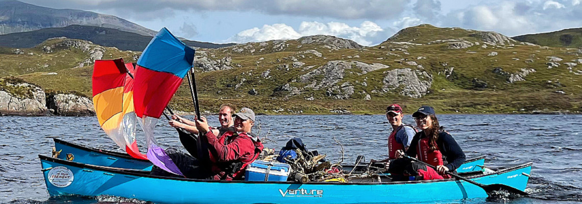 canoe expedition in the assynt area of scotland. people in canoes rafted together and making use of a canoe sail to help speed them along.