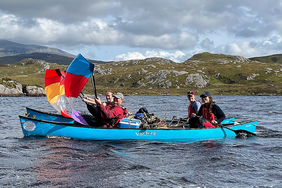 a group of people on an expedition, their canoes rafted together and making use of a tail wind by using canoe sails to speed them along.