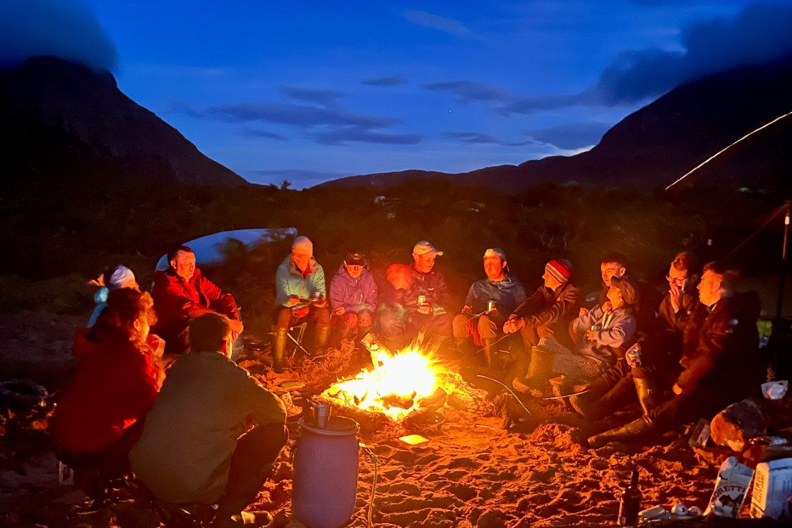 a group of work colleagues around a campfire in the evening having fun at end of a challenging day