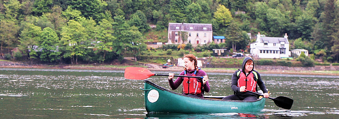 2 young people Canoeing on a calm Loch Long, west coast of scotland, smll houses in the background