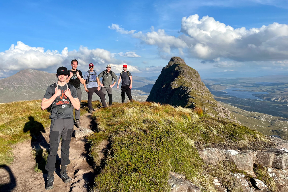 a group of adults reach the summit of mountain suilven on sunny day
