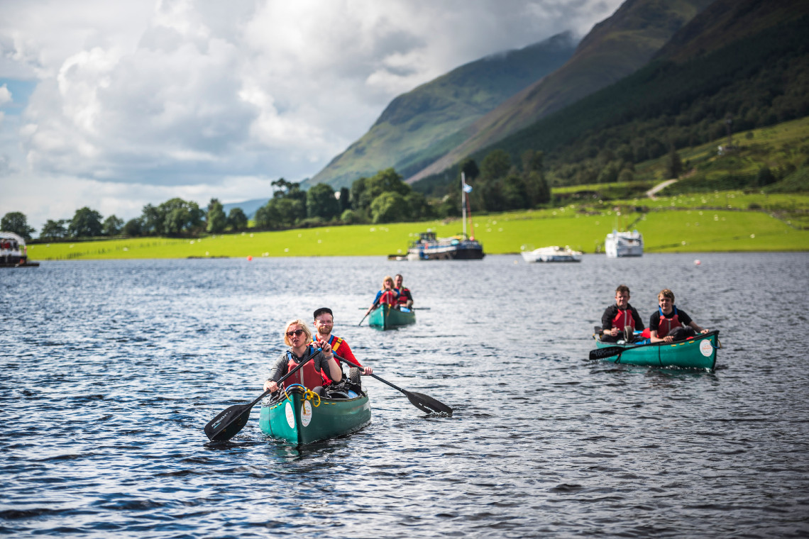 a group of people canoeing on a highland loch, with hilly, green background