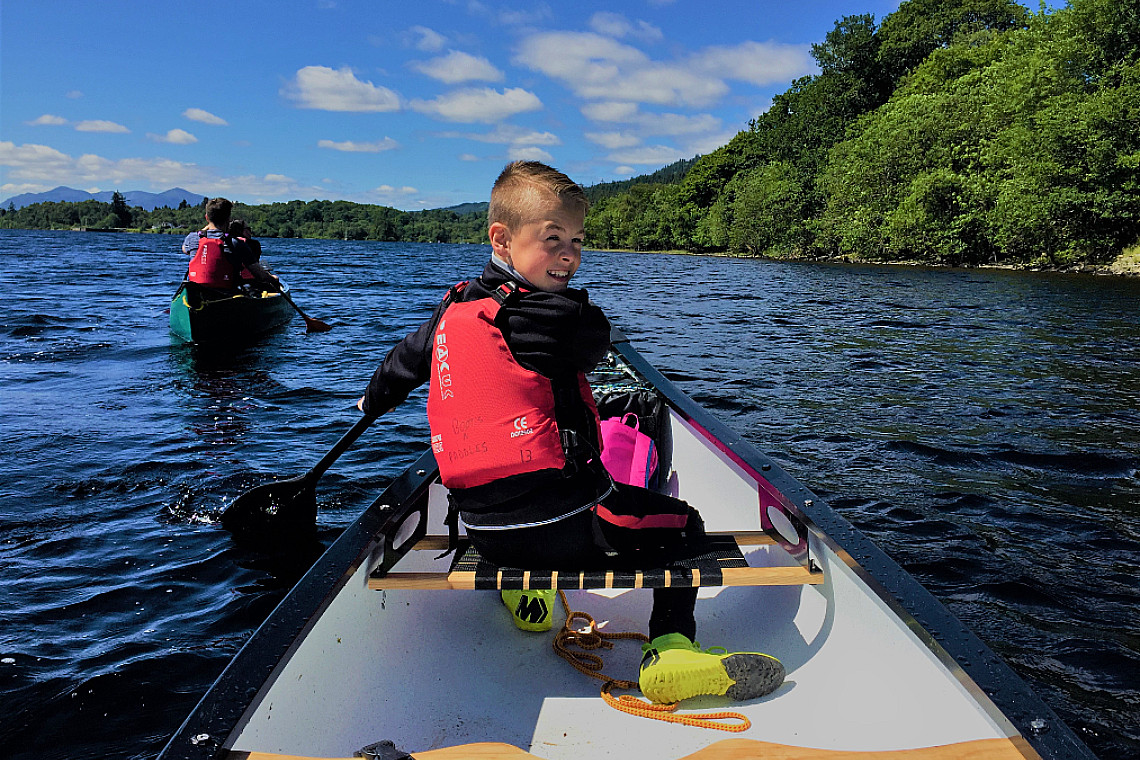 a young person sitting at the front of a canoe looking back at the camera
