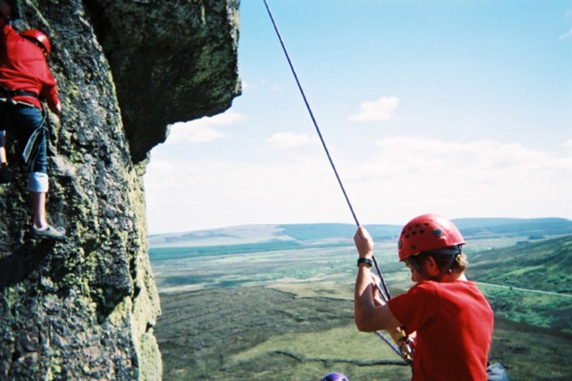 someone abseiling from a rock with great views as a background