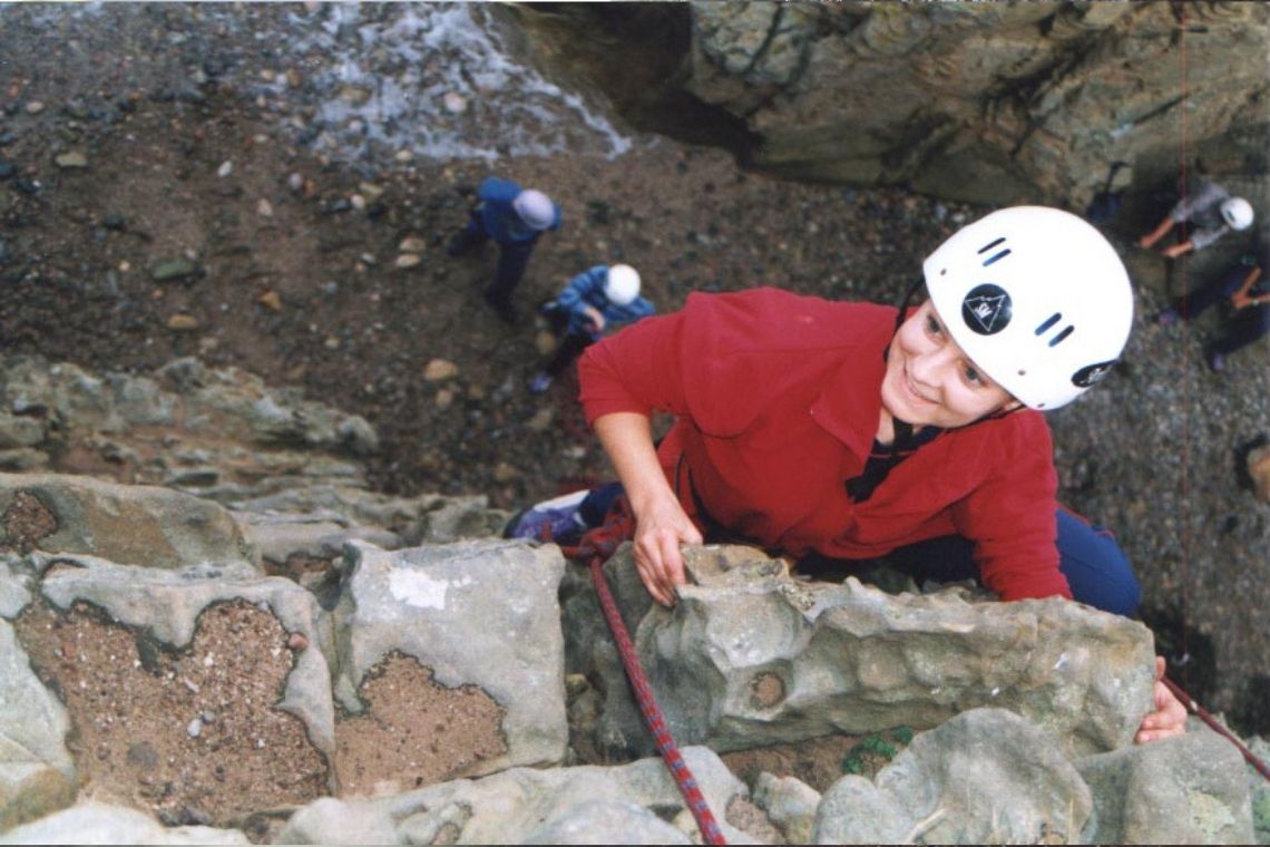 a young person reaches the top of a crock climb with big smile on face