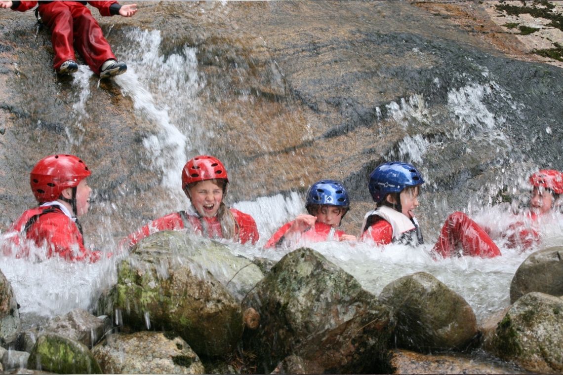a group of young people sitting and splashing in a river pool when gorge walking