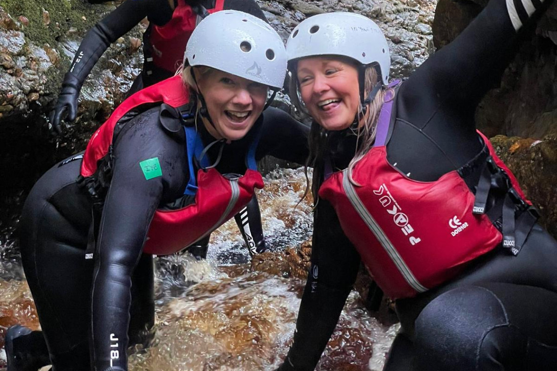 2 ladies in helmet and wetsuits smiling as they take part in a gorge walking session