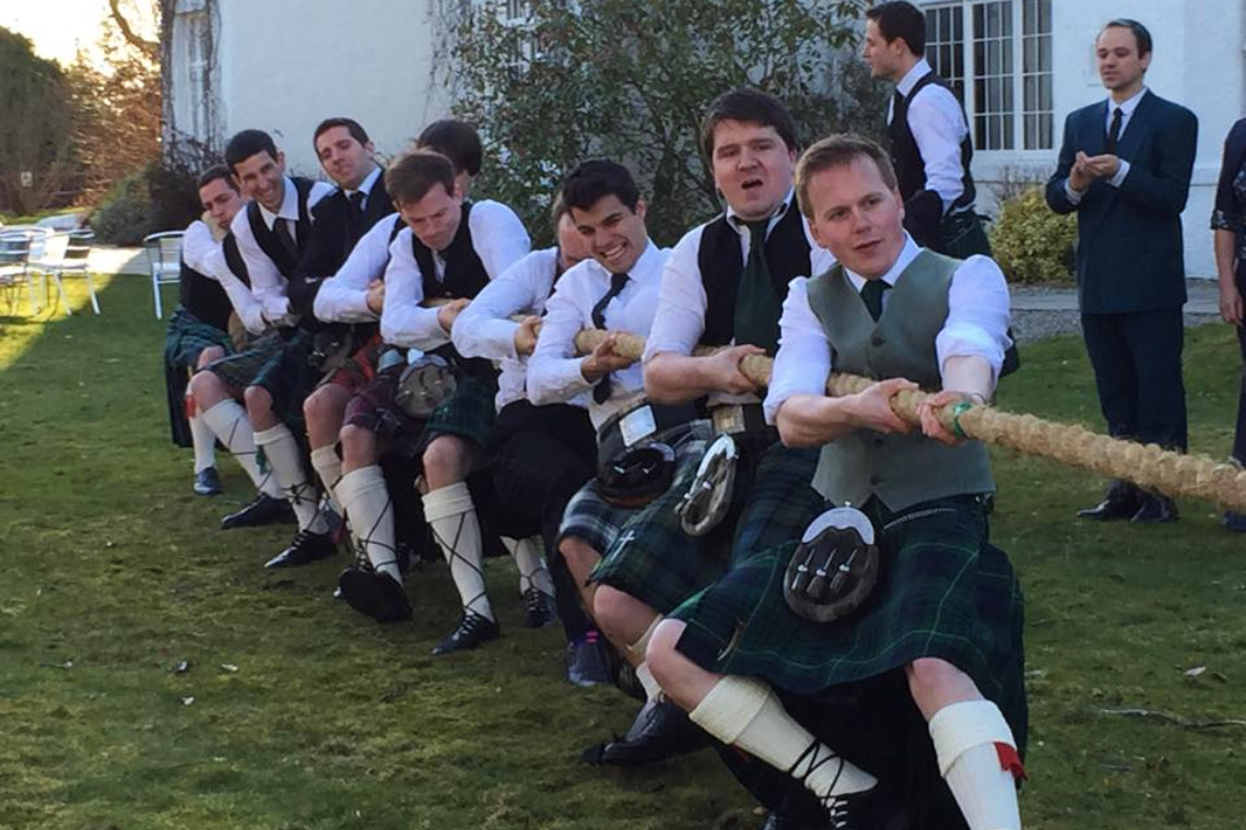 a group of kilted men taking part in a tug of war at a highland wedding event at achnagairn house near inverness