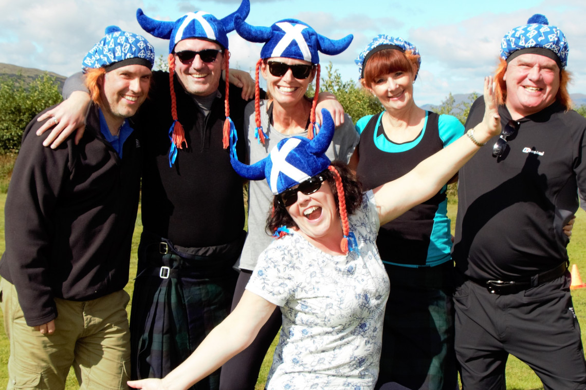 a smiling group of people, 2 with novelty, horned scottish hats posing for the camera after a highlang games event