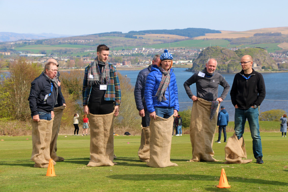 a group of adults standing in sacks, getting ready to race in a sack race during a fun highland games event