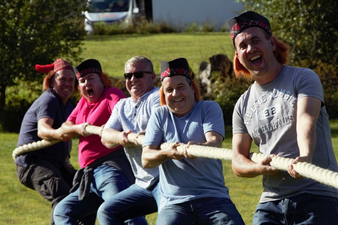 A group of men taking part in a tug of war as part of a highland games event. all laughing and smiling.