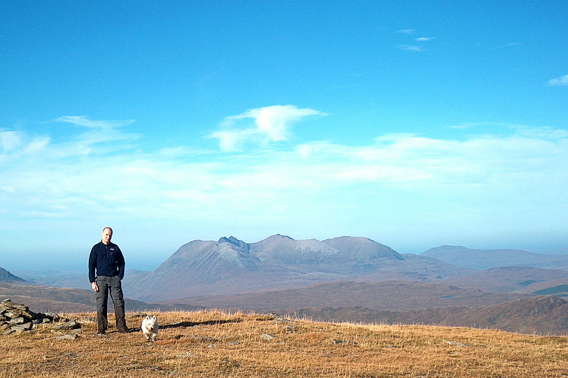 a lone walker with wee westie dog walking in the fannich mountains on glorious sunny day