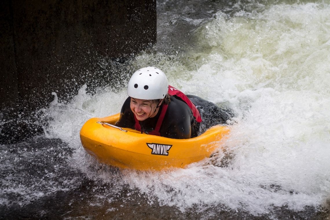 a lady with a big smile on her face as she rides a rapid on the river feshie near aviemore, during a white water river sledging session