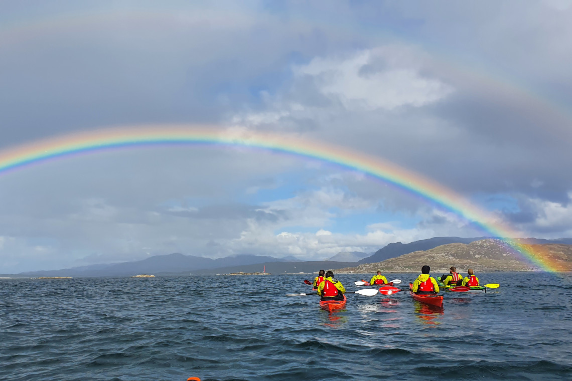 sea kayakers paddling under a rainbow on the west coast of scotland