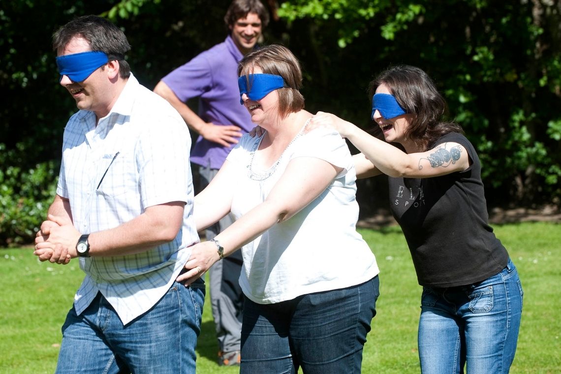 a group of 3 people holding on to each other as they try to find their way blindfolded, during a team challenge event