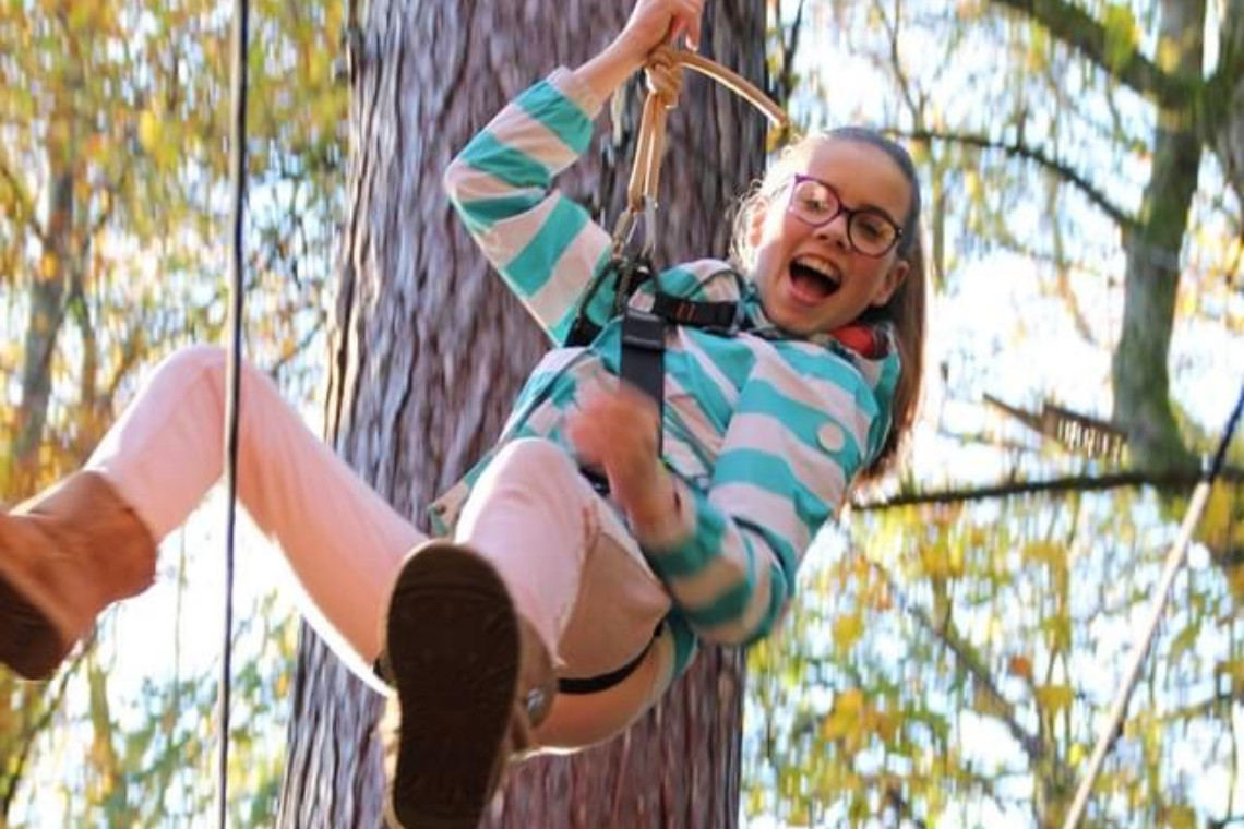 young girl laughing as she ziplines while at treezone treetop adventure course