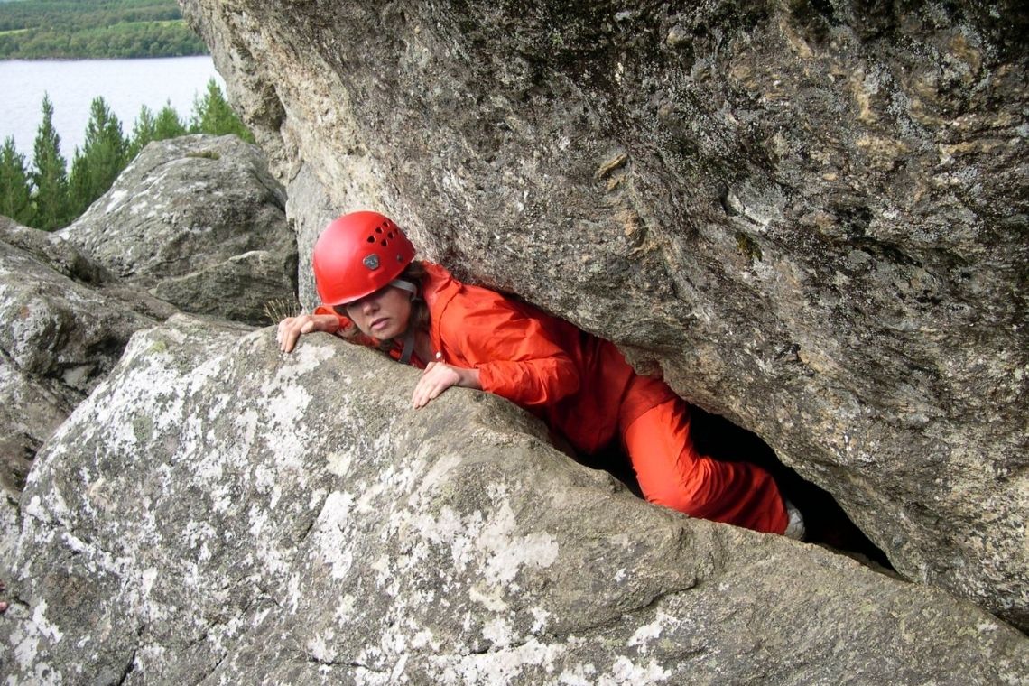 young person squeezing through a tight space between 2 large rocks while weaseling