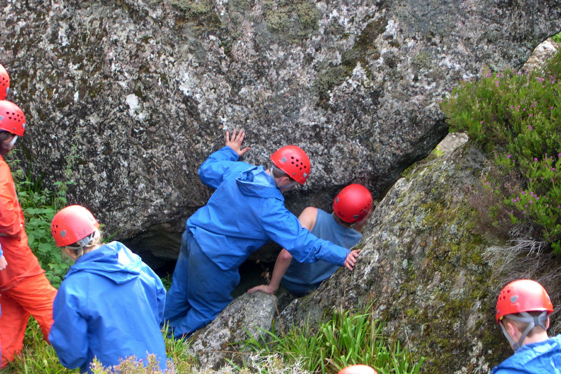 young people descending into a hole under large rocks while weaseling
