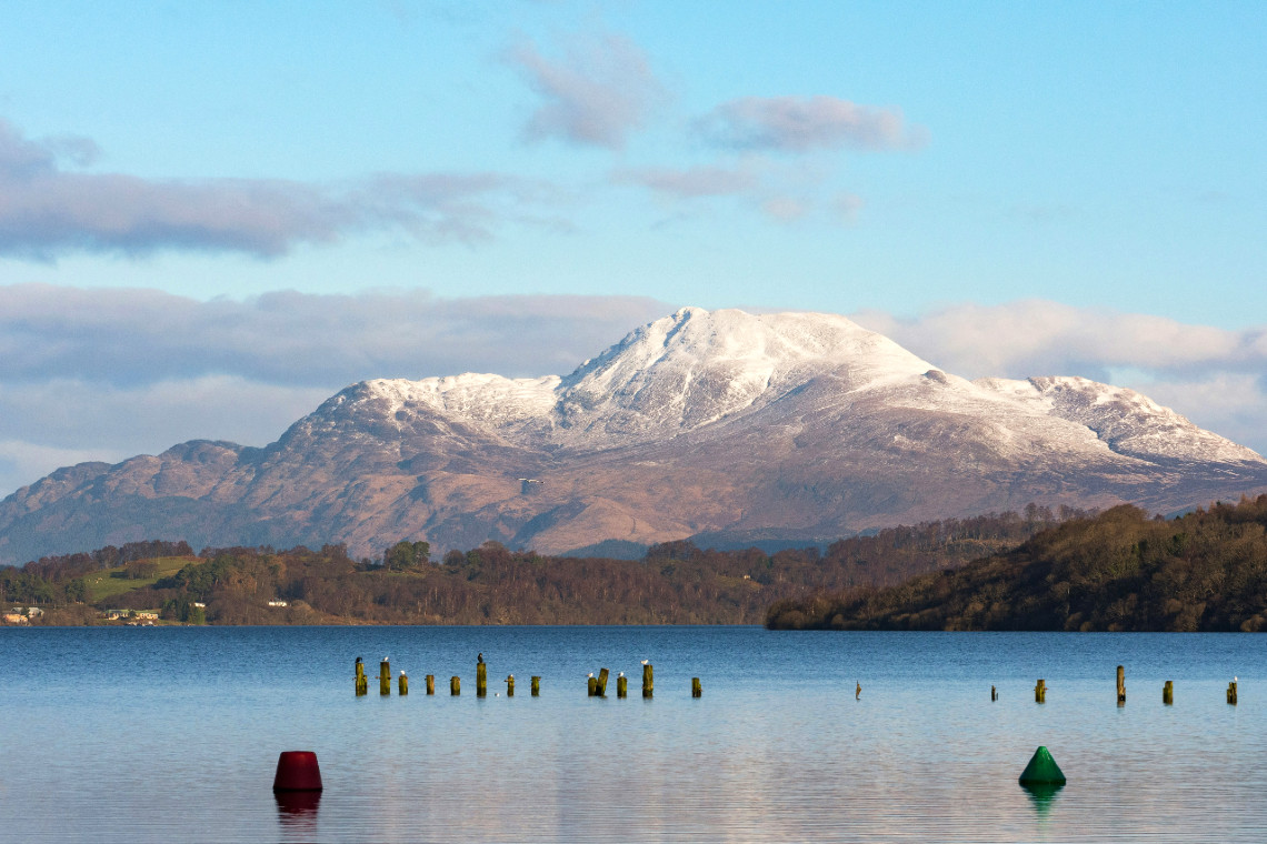 a snowcapped ben lomond with calm waters of loch lomond in the foreground