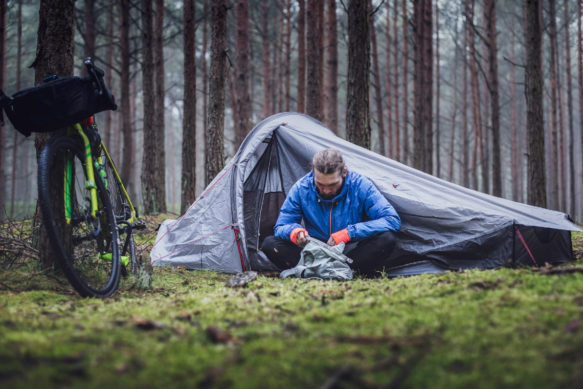 a man sitting by his tent with bike against the tree. Photo by Marek Piwnicki on Unsplash
