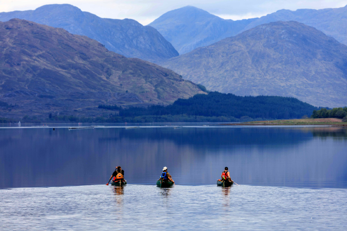 3 canoes paddling on loch tay with awesome mountainous backdrop and calm waters
