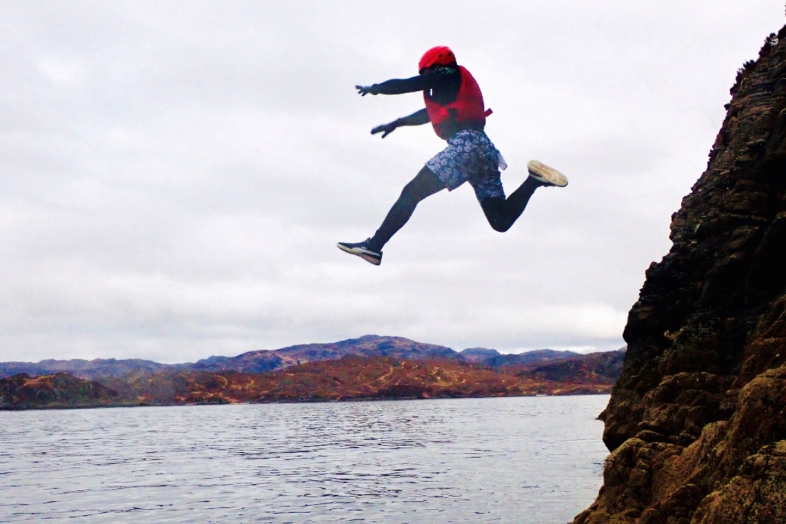 a person jumping from a clliff into the sea on a coasteering activity experience near fort william