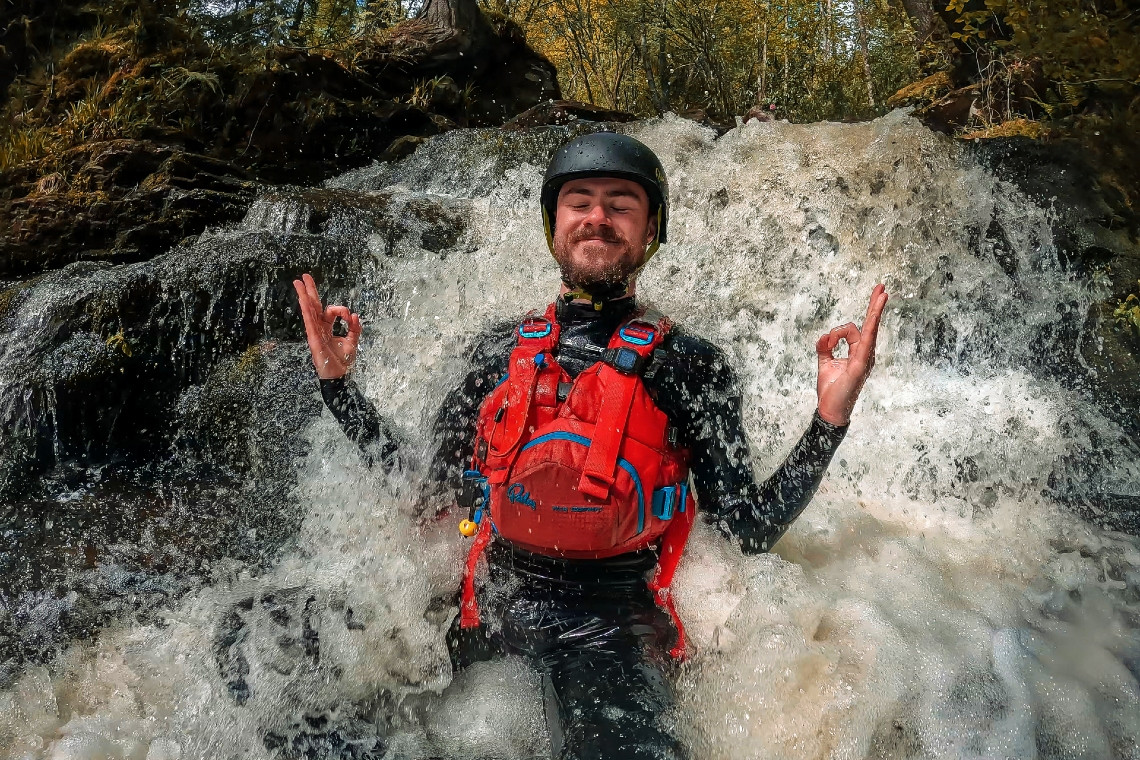 a man sitting pretending to meditate (with a smile on his face) as he sits in a small waterfall during a gorge walking session