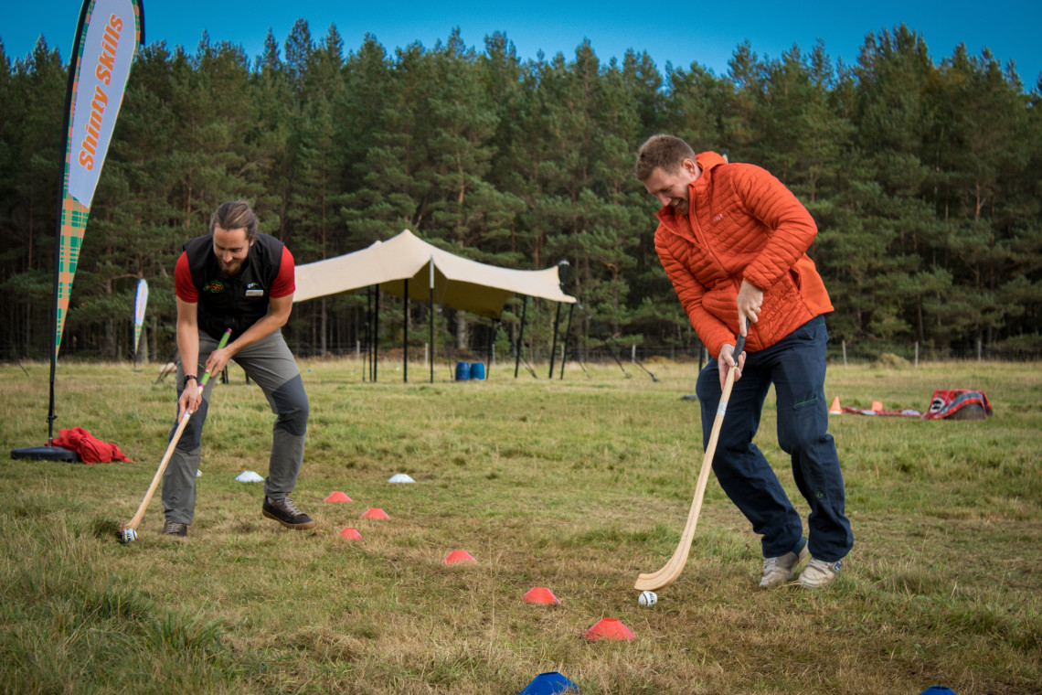 2 adults playing shinty as part of a mini highland games event