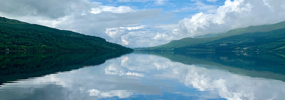 looking along the length of a calm loch tay, clouds reflecting off the water.