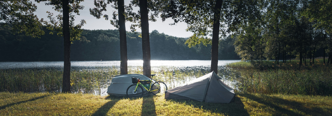 A tent pitched by a picturesque loch on a bike packing trip, bike leaned against a tree.