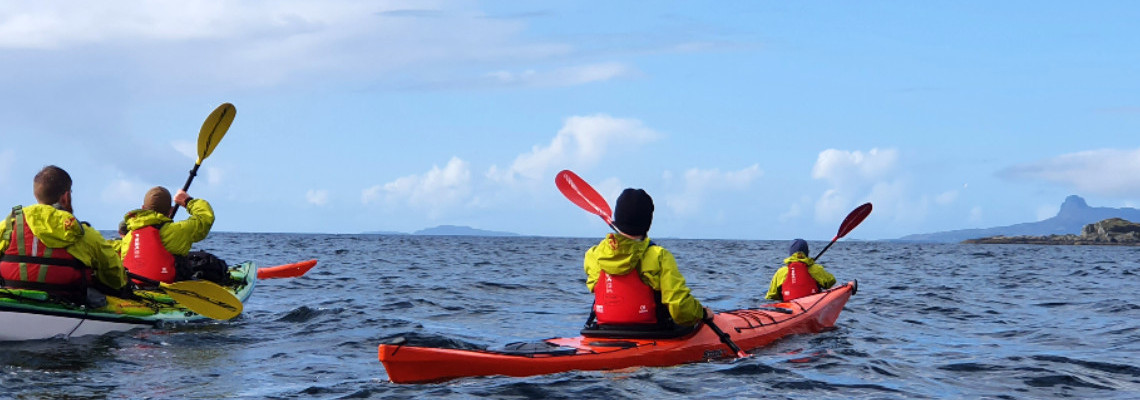 sea kayakers paddling on west coast of scotland on sunny day with blue skies, islands in distance in background
