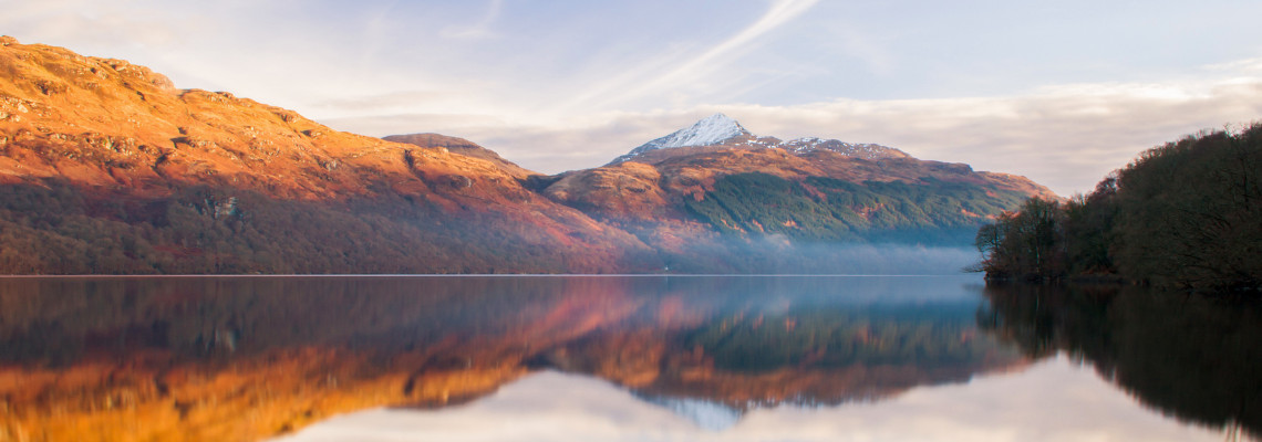 a view of stunning calm waters of loch lomond with snow capped ben lomond in the background